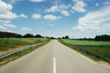 Otoyol bomboş. Güneşli yaz manzarası. Asfalt kırsal sokak. Çevrede yeşil alanlar. Mavi gökyüzü arka planı. Huzurlu sürüş sahnesi. Ufuk kaybolan nokta çizgisi.