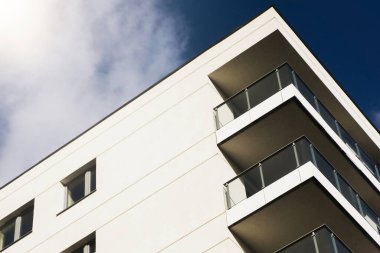 Modern bina cephesi. Güneşli konut mimarisi. Temiz beyaz duvar. Cam balkon tasarımı. Çağdaş gayrimenkul. Yeni apartman bloğu. Kentsel konut tarzı. Arkaplanda açık gökyüzü.