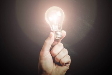 El ele tutuşan ampul. Kavram ve fikir geçmişi. Parlak ampul siyahta izole edilmiş. Parlayan ampulü tutan parmaklar. 