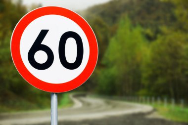 Arkasında ağaçlar olan hız limiti tabelası. Saatte maksimum 60 kilometre. Yol arka planında güvenlik.