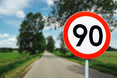 Arkasında ağaçlar olan hız limiti tabelası. Saatte maksimum 90 kilometre. Yol geçmişinde güvenlik var. Beyaz, yuvarlak, kırmızı sınır çizgisi. Trafik cezası geçmişi. Hız iyi..