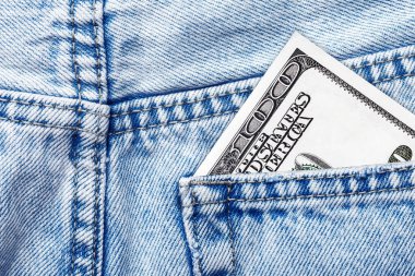 Kapalı kot pantolonun cebinde 100 dolarlık banknot var. Kumaşta parlak, temiz dikişler var. Zenginlik, tasarruf, gelir, harcama veya görünür parayla günlük yaşam tarzı sembolü.