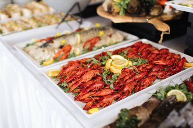 Limon ve otlarla süslenmiş ıstakoz tepsileriyle servis büfesi. Düğün ya da etkinlikte nefis deniz ürünleri sunumu. İçerideki şenlikli yemek masasında sergilenen taze ve renkli yemekler..