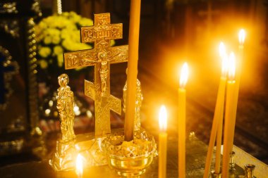 Ortodoks anma mumları. Parlayan haçlı ve simgeli altın mum ışığı. Ruhani ritüel sahnesi. Kilise dua atmosferi. Ilık ışık yansımaları. Din ve hatıra. Huzurlu kutsal an.