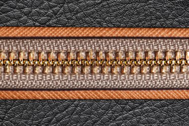 Deri fermuar dokusuna yakın çekim. Kahverengi kenarlı siyah deri kumaş. Parlak altın fermuar detayı. Moda materyali makro arka planı. Zarif dikişli tasarım. Endüstriyel aksesuar bileşeni.