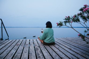 Rıhtımda telefonlu bir kadın kuşların fotoğraflarını çekiyor.