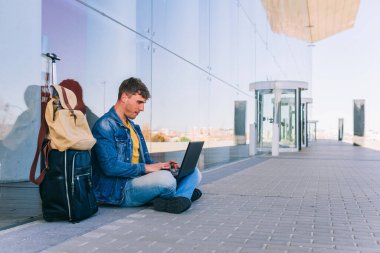 Havaalanında oturan genç işadamı dizüstü bilgisayarıyla uçağını bekliyor..