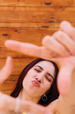 Güzel bir kadının dikey yakın plan fotoğrafı. Öpücük atıyor ve elleriyle bir çerçeve yaratıyor.