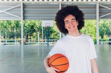 Sahada sıradan kıyafetlerle gülümseyen genç bir basketbolcunun portresi.