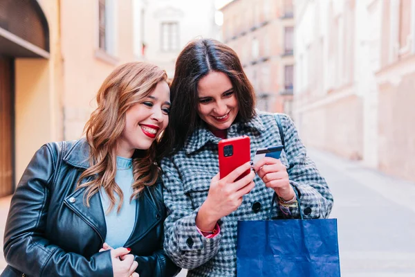 Two Female Friends Using Phone While Carrying Shopping Bags Street — Stock Photo, Image