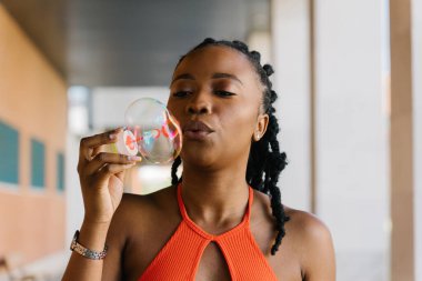 Genç bir kadın şehir ortamında oyuncakla sabun köpüğü yapıyor, eğleniyor ve eğleniyor.