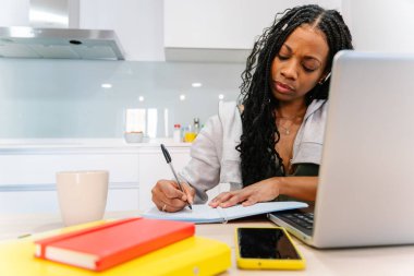 Genç bir kadın ev mutfağında çalışırken dizüstü bilgisayar kullanıyor.