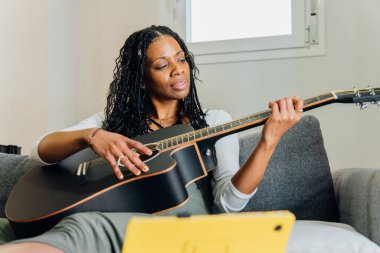 Müzisyen çevrimiçi kurslar kullanarak gitar çalmayı öğreniyor, akorları çalışıyor ve dijital tablette özel ders seyrediyor.