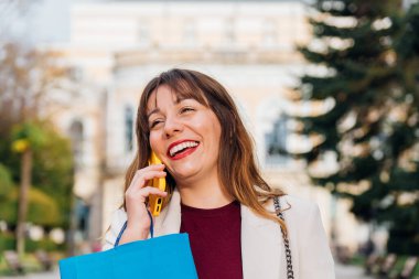Alışveriş çantalı mutlu kadın akıllı telefondan konuşuyor başarılı bir alışveriş gezisinden sonra keyifli bir sohbet ediyor.