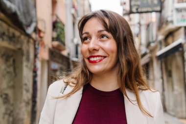 Şehir caddesinde yürürken gülümseyen genç bir iş kadını. Gezintiden zevk alıyor ve etrafa bakıyor.