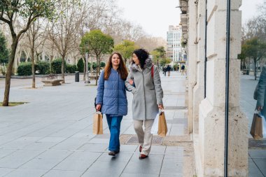 Anne ve kızı başarılı bir alışveriş çılgınlığından sonra el ele yürüyorlar.