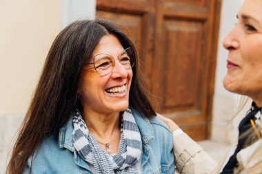 İki neşeli olgun kadın birlikte dışarıda eğleniyor, bir kahkaha ve bir bağ anı paylaşıyorlar, arkadaşlığın ve birlikteliğin sıcaklığını somutlaştırıyorlar.