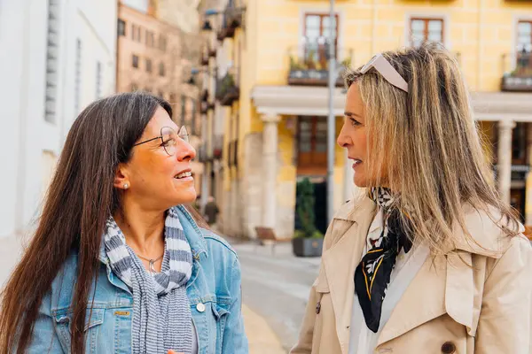 İki olgun bayan arkadaş şehir gezintisinden zevk alıyor, dostça sohbet ediyor ve bir şehir zeminine karşı gülümsemelerini paylaşıyorlar.