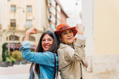 İki neşeli son sınıf öğrencisi kadın, arka arkaya şehir sokaklarında kaslarını esnetiyor ve gülümsüyor, kadınların güçlenmesini ve aktif yaşlanmalarını kutluyorlar.