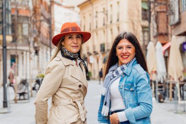 İki neşeli olgun kadın, hareketli bir şehir caddesinde şık günlük giysiler içinde yürürken ve güneşli bir günde mutluluk saçarken birlikte eğleniyorlar.