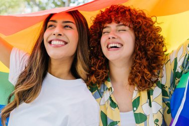 Igbtq + gurur ve eşitliği kutlarken büyük bir gökkuşağı bayrağı tutan iki neşeli kadın, canlı toplulukları içinde çeşitlilik ve kapsama ruhunu somutlaştırıyorlar.