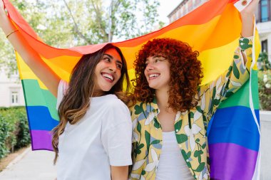 Gökkuşağı bayraklı arkadaşlar lgbtq gururunu kutluyorlar, şehrin sokak buluşması sırasında neşeli ifadelerle birlikte duruyorlar, çeşitliliği ve birliği temsil ediyorlar.