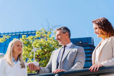 İş adamı, meslektaşlarıyla yenilenebilir enerji stratejilerini tartışırken elinde küçük bir rüzgar türbini tutuyor ve sürdürülebilir uygulamalara olan bağlılıklarını gösteriyor.