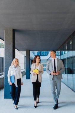 Parlak ofis binasının dışında iş birliği yapan iş adamları, modern şehir ortamında birlikte yürürken proje detaylarını tartışıyorlar, profesyonel kıyafetler giyiyorlar.