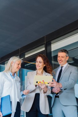 Profesyonel meslekdaşlar tablet üzerindeki dijital verileri inceliyor, çağdaş kurumsal dışa yakın yerlerde birlikte çalışıyor, stratejik planlama oturumu sırasında olumlu etkileşimi paylaşıyor