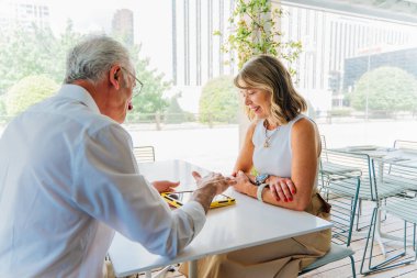 Modern bir restoranda masada oturan iki kıdemli iş adamı, önemli iş konularını tartışırken bir tablet ile meşgul oluyorlar, işbirliği ve strateji gösteriyorlar.