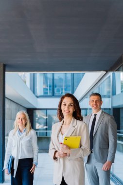 Çağdaş bir ofis binasının koridorunda birlikte duran, takım çalışması, başarı ve profesyonelliği kurumsal bir ortamda aktaran bir grup kendinden emin iş adamı.
