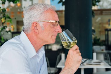 Kıdemli şarap garsonu, bir restoranın iğrendiği yerde oturmuş şarap tatma deneyimine dalmışken aromatik beyaz şarabın tadını çıkarıyor.