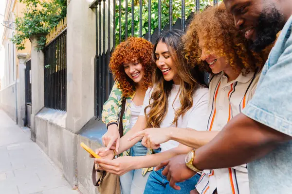 Aralarında öğrenci ve pazarlama müdürünün de bulunduğu dört neşeli genç arkadaş, bir akıllı telefonun etrafında toplanmış, şehir ortamında neşeli bir anın keyfini çıkarırken işaret ediyor ve gülüyorlar.