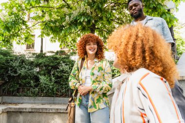 Üç genç öğrenci, iki kız ve bir oğlan, birlikte dışarıda duruyorlar, dostça bir sohbet içindeler, keyifli şehir ortamının tadını çıkarıyorlar.