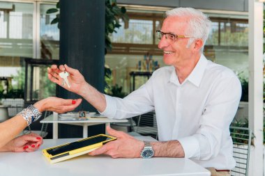 Üst düzey emlakçı, tabletle kontrat imzaladıktan sonra ev anahtarlarını müşteriye veriyor, yeni mülk alımı ya da kira sözleşmesi için anlaşma yapıyor.