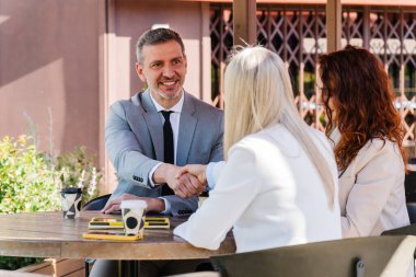 İş ortakları açık bir kafede bir masada otururken el sıkışıyor, başarılı bir anlaşmayı kutluyor ya da anlaşma yapıyor.