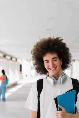 Üniversite koridorunda elinde kitaplarla, kulaklık takmış, derse hazır mutlu bir üniversite öğrencisi.