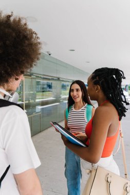 Farklı öğrencilerden oluşan bir grup kampüste sohbet ediyor, fikirleri ve bilgileri paylaşıyor, ellerinde defterler tutuyorlar.
