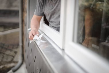 Beyaz bir gencin eli pencerenin çerçevesini silerken yenilemelerin yapıldığı bir odada duruyor, seçici bir odak noktasıyla yan görüntü..
