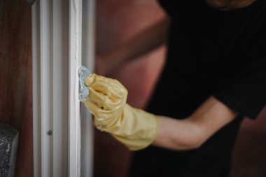 Sarı eldivenli beyaz bir erkeğin elleri, kırmızı duvarların arka planına karşı sünger ve pencere çerçevesi sabunuyla yıkanır, seçici bir odak ile yakın plan yan görüş. Ev yenileme konsepti, pencere çerçeveleri.