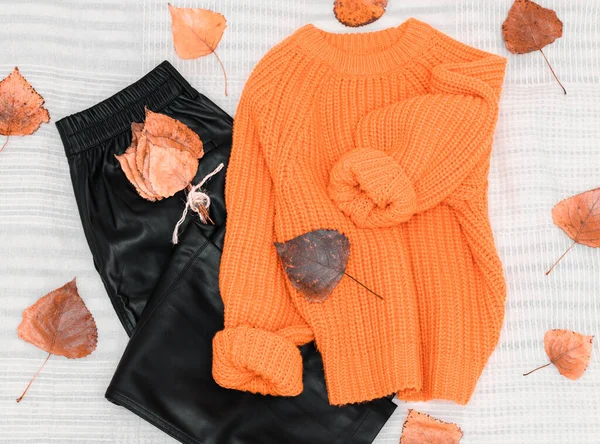 オレンジのニットセーター 黒い革のパンツ 秋のポプラの葉がベッドの上から白いベッドスプレッド クローズアップビューで周りに散らばっている — ストック写真