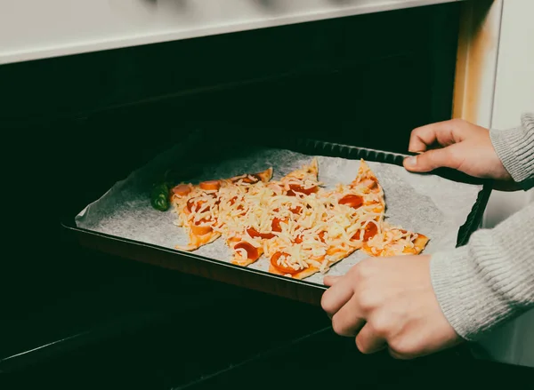 Children hand lays down a baking dish with a Christmas tree pizza in the oven, side view close-up. The concept of preparing for Christmas and New Year.