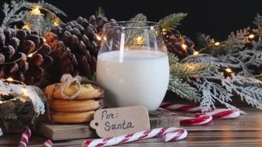 Noel Baba için bir nota iliştirilmiş jüt iplikli bir bardak süt koni ve ahşap bir masanın üzerinde yanan bir çelenk ile birlikte bir Noel ağacının altında yatıyor..