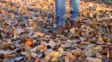 Mavi kotlu ve kahverengi çizmeli genç bir adamın bacakları sonbaharda solmuş yeşilliklerde yürür, yavaş çekimde aşağıdan yakından bakar..