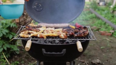 Genç beyaz adam, evin arka bahçesinde ızgara biftek ve biberli ızgara ızgara ile çiğ tavuk eti yayar. Yavaş çekimde sağa doğru izler..