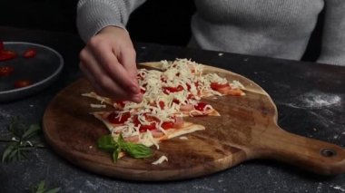 Kafkasyalı ergen kız, hamur hamuruna noel ağacı şeklinde mozzarella peyniri serpiştirir. Koyu çimento masasında malzemelerle dururlar. Yan görüntüyü yavaş çekerler. Bayram pizzası pişirme kavramını adım adım kavrayın..