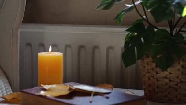 房间里靠近床边的桌子上放着一本褐色的书 上面散落着秋天的白杨树叶和一根黄色的蜡烛 一边慢慢地近距离观看 一边放大 — 图库视频影像
