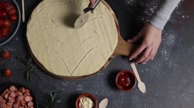 Kafkasyalı genç bir kızın elleri bıçakla kesilmiş halde pizza hamurunun üzerinde ay şeklinde bir Noel ağacı şeklinde koyu çimento masasında malzemelerle duruyor, üst tarafı yavaş çekimde. Tatil pizzası pişirme kavramı, adım adım..