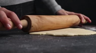 Kafkas ergen kız elleri ve merdaneyle yuvarlak pizza hamuru yuvarlıyor. Koyu çimento masasında dururken, aşağıdan yavaş çekimde yakın çekim. Bayram pizzası pişirme kavramı, adım adım..