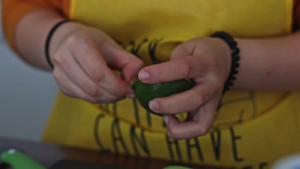 Руки Молодої Білої Жінки Жовтому Фартуху Чистить Половину Авокадо Стоячи — стокове відео